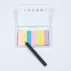 白色便條盒打開後的特寫，內部裝有七種粉彩色系（粉紅、黃、天藍、粉紫、嫩綠、橘、紫）的長條型標籤便條紙，盒內配有一支黑色迷你原子筆，正在黃色便條紙上畫出流暢的線條。
