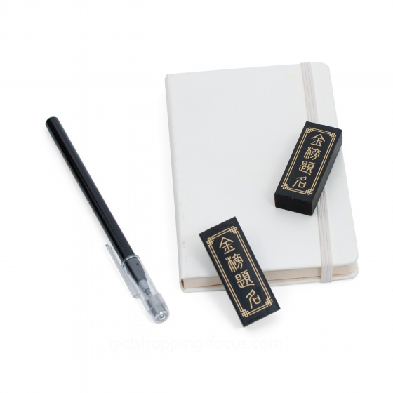 印有金色「金榜題名」燙金字樣的墨條造型黑色橡皮擦，斜放在白色筆記本旁展示。